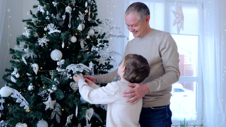 Twinkling lights of Christmas tree father and son celebrate holiday season radiating positive energy and deep familial love. Father and son enjoy holiday cheer bond strengthened by shared happiness.の写真素材