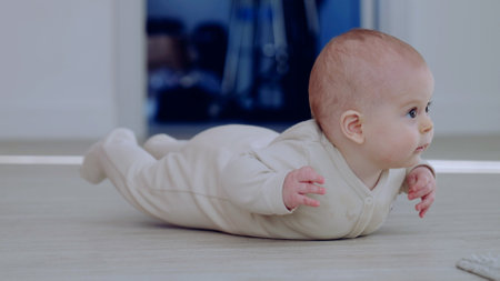 Sweet baby in a beige onesie lifts head and chest on the floor, showing growth and coordination,...