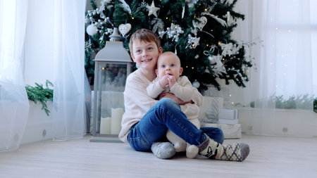 Two brothers making memories by the christmas tree, surrounded by presents and holiday decor, in a cozy and joyful setting. A day with family before Christmas. New Years Eve with familyの写真素材
