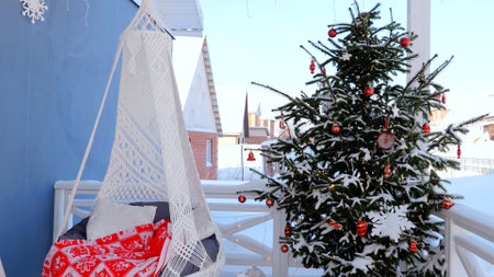 Festive and cozy balcony scene with a snow covered christmas tree adorned with red ornaments and...