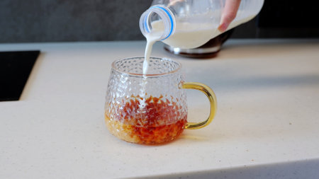 Human hand pours milk into cup of black tea simple process of making classic tea with milk. Milk swirls into cup of black tea rich flavor and creamy texture of this beloved drink delicious treat.