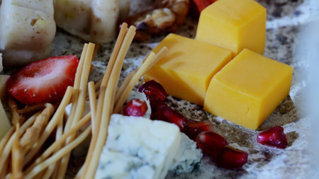 Rustic wooden board displaying scattered breadsticks, pomegranate seeds, ripe strawberries, and artisan cheese varieties in elegant compositionの写真素材