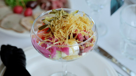 Professional waiter wearing black gloves serving russian salad, featuring diced vegetables, meat,...