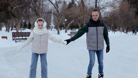 Loving couple skating hand in hand across frozen rink, sharing intimate moment amid snow covered...