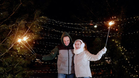 Romantic couple embracing, waving sparkling fireworks during festive nighttime celebration, glowing...
