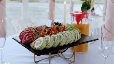 Fresh spinach, beet, and shrimp rolls garnishing slate platter, nestled near champagne glasses and juice pitcher, showcasing gourmet appetizer eleganceの写真素材