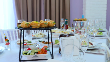 Elegant restaurant table featuring golden profiteroles, canapes, appetizers, and empty wine glasses,...