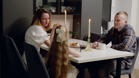 Caucasian family sharing christmas dinner, savoring warm beverages and festive treats by soft candlelight, creating intimate holiday moment at homeの写真素材