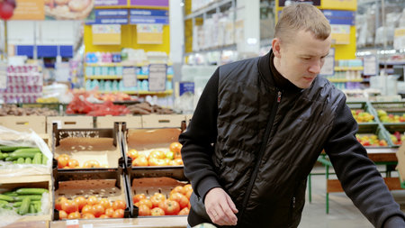 Man choosing vegetables in supermarket, shelves with vegetables. Customer selecting from a variety of fresh vegetables in the supermarkets grocery department while shopping for groceriesの写真素材
