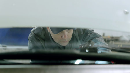 Professional mechanic fixing car windshield with specialized tools in auto service workshop, wearing uniform and protective gearの写真素材
