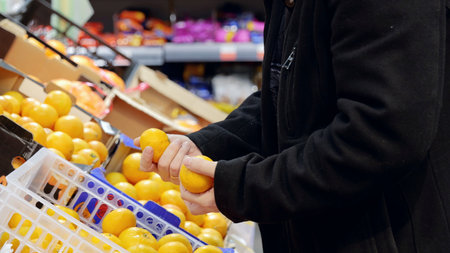 Careful hands picking ripe, colorful oranges from fresh produce display, highlighting mindful selection of nutritious fruit at grocery storeの写真素材