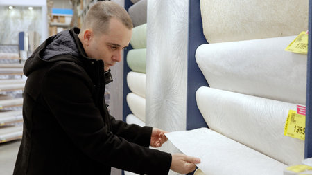 Customer selecting wallpaper samples, comparing patterns and textures while planning home interior design renovation in hardware store showroomの写真素材