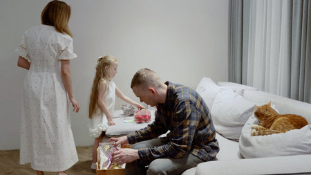 Family members preparing holiday decor from vintage wooden container, ginger cat napping nearby on living room couch, mother moving away in backgroundの写真素材