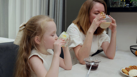 Loving mother and daughter enjoying nutritious breakfast, sharing milk and warm smiles in bright...