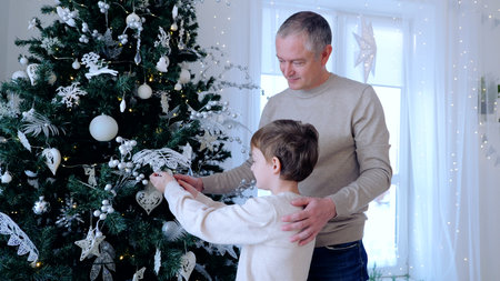 Father and son carefully add silver ornaments to their christmas tree as they put on the final touches. A day with family before Christmas. New Years Eve with familyの写真素材