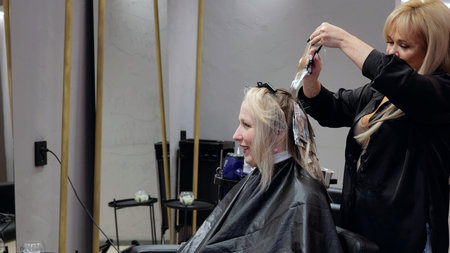Hairdresser using foil highlights to bleach a blonde womans hair in a contemporary salon, achieving...