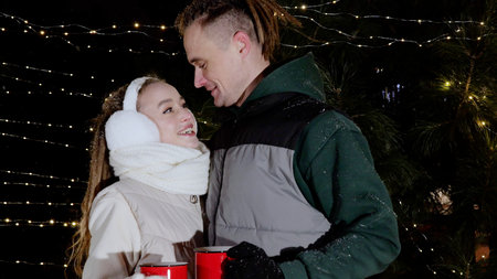 Winter clad lovers sipping steaming beverages, wearing cozy earmuffs and gloves, sharing warm smiles...