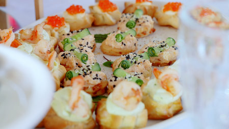 Elegant canapes arranged on a white plate, featuring toppings like shrimp, cucumber, sesame seeds, and creamy spread, perfect for festive gatheringsの写真素材