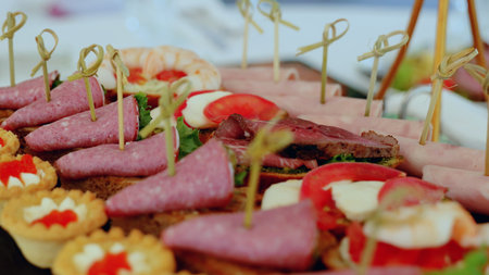 Close up of various canapes arranged on a platter, showcasing a mix of salami, ham, roast beef, shrimp, and fresh toppings, ready to be served at a catered eventの写真素材