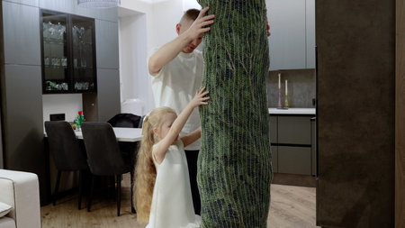 Family decorating living room, setting up faux pine tree together, sharing festive excitement while creating holiday memories at homeの写真素材