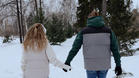 Couple walking hand in hand through snow covered park, sharing intimate moment amid winter landscape and bare treesの写真素材