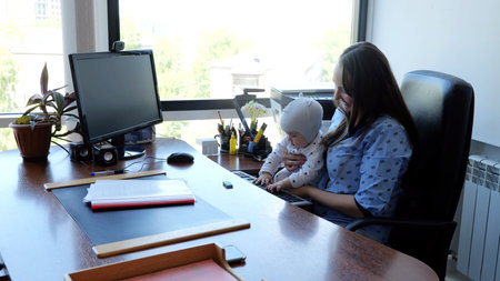 Working mother balancing work and family life, businesswoman typing at desk with baby on lapの写真素材