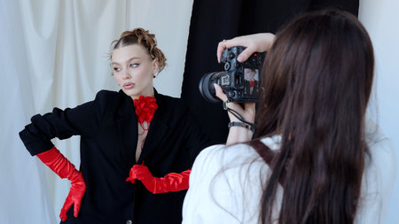 Fashion photographer taking pictures of a beautiful model wearing red gloves and a red flower choker, posing in a studio with black and white backgroundの写真素材