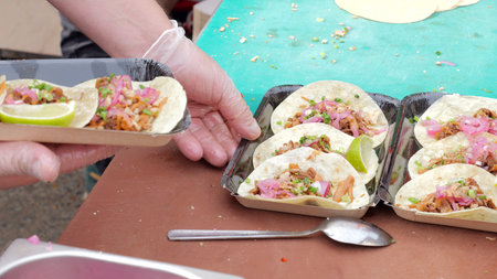 Tightly packed line of foil trays with ready tacos surrounded by utensils and condiments, Busy event food stand where staff prepare and arrange multiple taco portions for eager festival visitorsの写真素材
