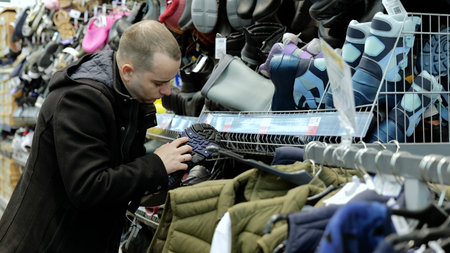 Male customer carefully examining trekking shoe sole, inspecting quality and materials while...