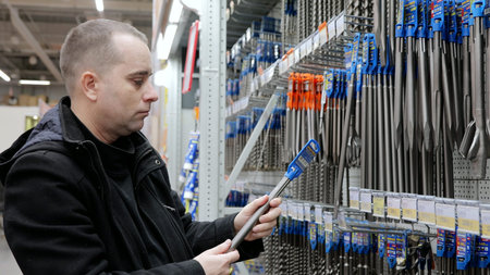 Construction worker examining drill bits at hardware store, comparing sizes and materials for...