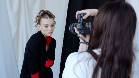 Professional photographer using digital camera while shooting fashion model, creating elegant studio portrait with dramatic lighting and dynamic poseの写真素材