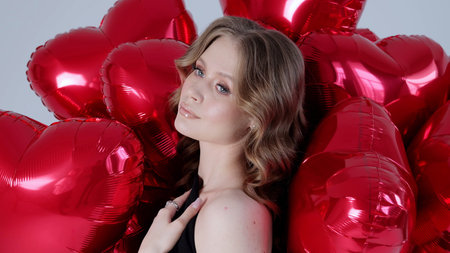 Blonde woman posing amid red heart shaped balloons, generating romantic valentines mood in professional studio setting with soft lightingの写真素材