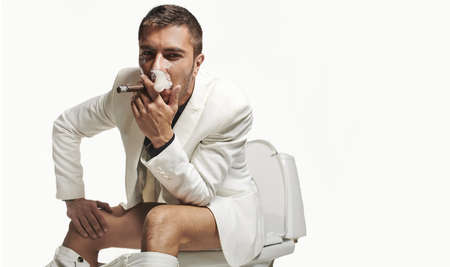 Fashion young man sitting on the toilet with cigarの写真素材