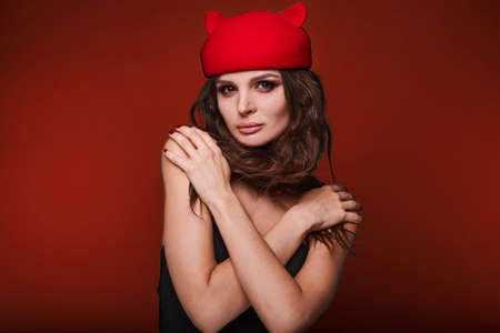 Beauty portrait of young swag woman with curly long hair in cat hat on red background in studio.の写真素材