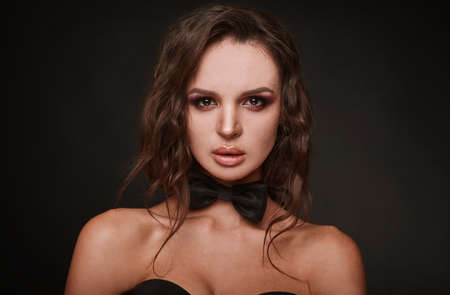 Beauty portrait of young swag woman with curly long hair in bow-tie on black background in studio.の写真素材