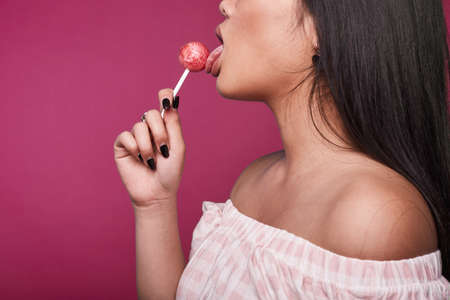 Fashion swag portrait of beautiful elegant asian woman in pink dress with lolipop on bright backgroundの写真素材