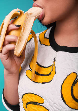 Fashion swag close-up portrait of beautiful elegant asian woman eating banana on bright backgroundの写真素材