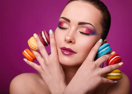 Beauty glamor fashion model girl with colourful makeup and manicure taking colorful macaroons. Studio shoot.Diet,dieting concept. Sweets.の写真素材