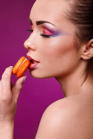 Beauty glamor fashion model girl with colourful makeup and manicure taking colorful macaroons. Studio shoot.Diet,dieting concept. Sweets.の写真素材