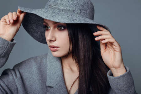 young fashion brunette woman beauty portrait posing in studio wearing in gray coat and hatの写真素材