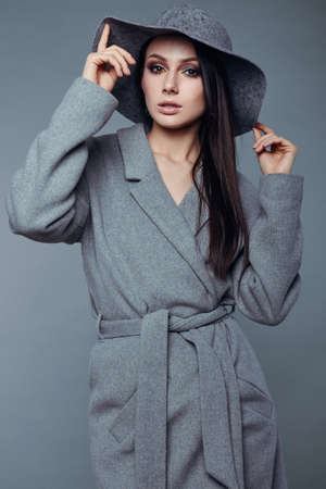 young fashion brunette woman beauty portrait posing in studio wearing in gray coat and hatの写真素材
