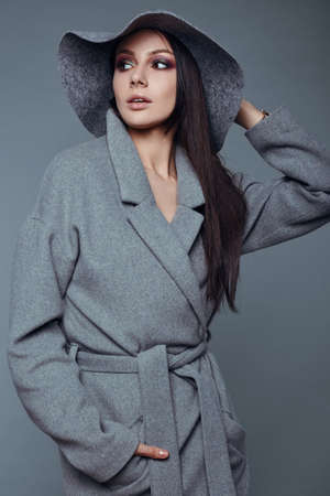 young fashion brunette woman beauty portrait posing in studio wearing in gray coat and hatの写真素材