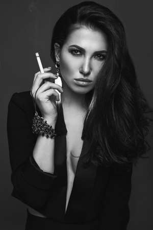 Elegant hot brunette woman smoking a cigarette on black background in studioの写真素材