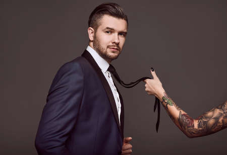 Portrait of elegant brutal man in a suit with a female hand holding a tie on a gray backgroundの写真素材