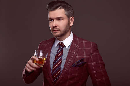 Portrait of elegant brutal man in a expensive wool suit with glass of whiskey on a gray backgroundの写真素材
