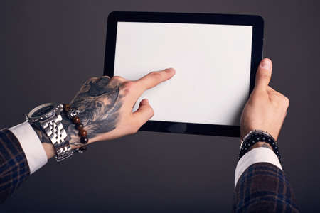 Close-up portrait of hands with a tattoo brutal man holding a tablet on a gray background