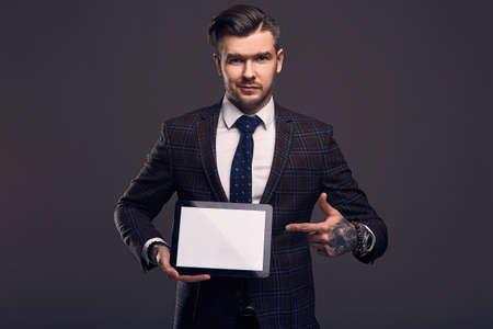 Portrait of a young elegant brutal man in an expensive suit with a tablet in hands on gray backgroundの写真素材