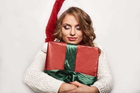 Portrait of a beautiful positive smiling blonde in a sweater and festive cap holding gifts isolated on white backgroundの写真素材