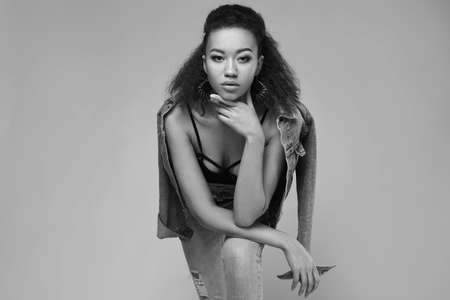 Portrait of glamor elegant black woman model in jeans and jacket posing on a gray background in studioの写真素材
