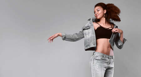 Portrait of glamor elegant black woman model in jeans and jacket posing on a gray background in studioの写真素材